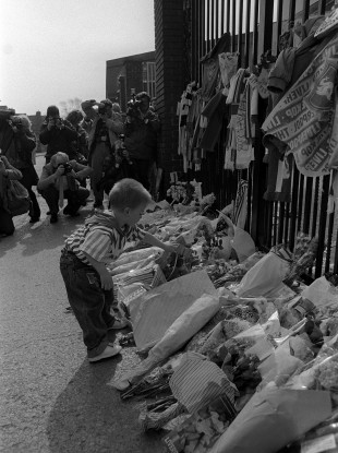 A boy adds a floral tribute at Anfield's Shankly Gates in remembrance of those who lost their lives.